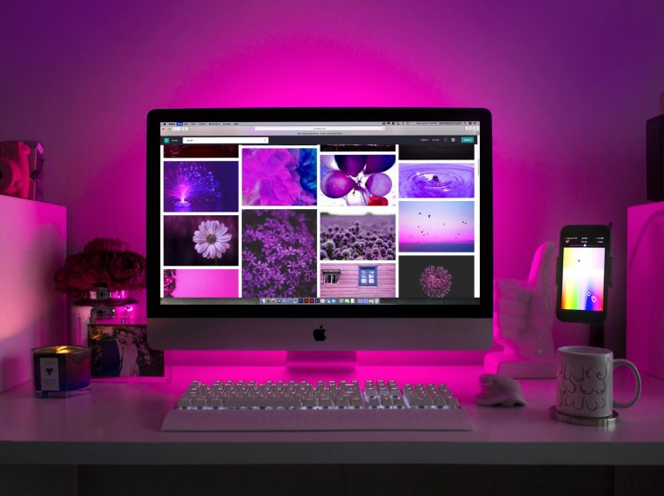 Modern desk setup with neon lighting and a desktop computer displaying colorful images.